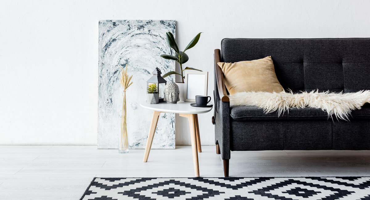 Black couch and black and white rug, next to a white end table against a white wall